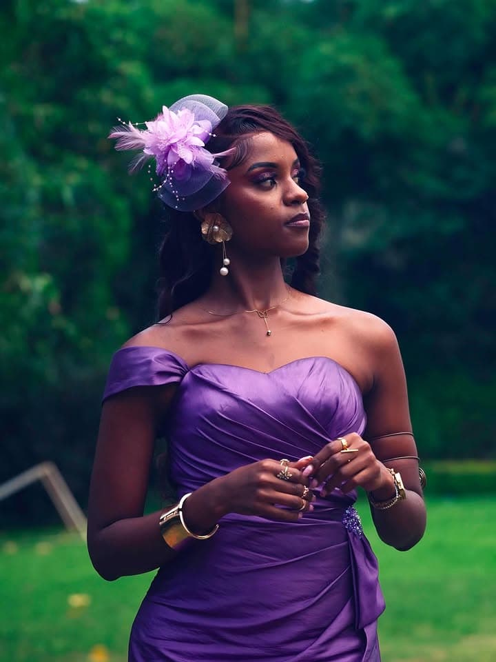 Woman wearing a draped purple off-shoulder dress and matching floral fascinator